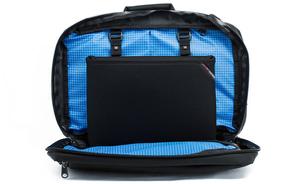 The rear main pocket of a Black 525 Ballistic exterior Western Flyer opened to reveal an Island (blue) 200 Halcyon interior with a Cache connected to the nylon loops sewn into the interior seam.